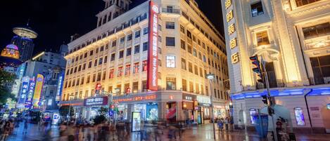 A historic building with multiple floors and a prominent corner entrance, surrounded by a bustling urban square with various shops and signs.