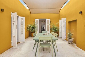 Uma área de refeições com mesa e cadeiras, plantas em vasos e uma porta com portões.
