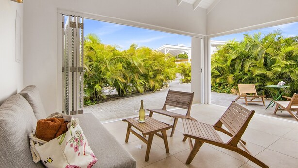 A spacious patio with wooden furniture, a bottle of wine, and a view of lush greenery. - Villa Grandi — three villas on one walled estate, for 16 guests in Otrobanda (Willemstad)