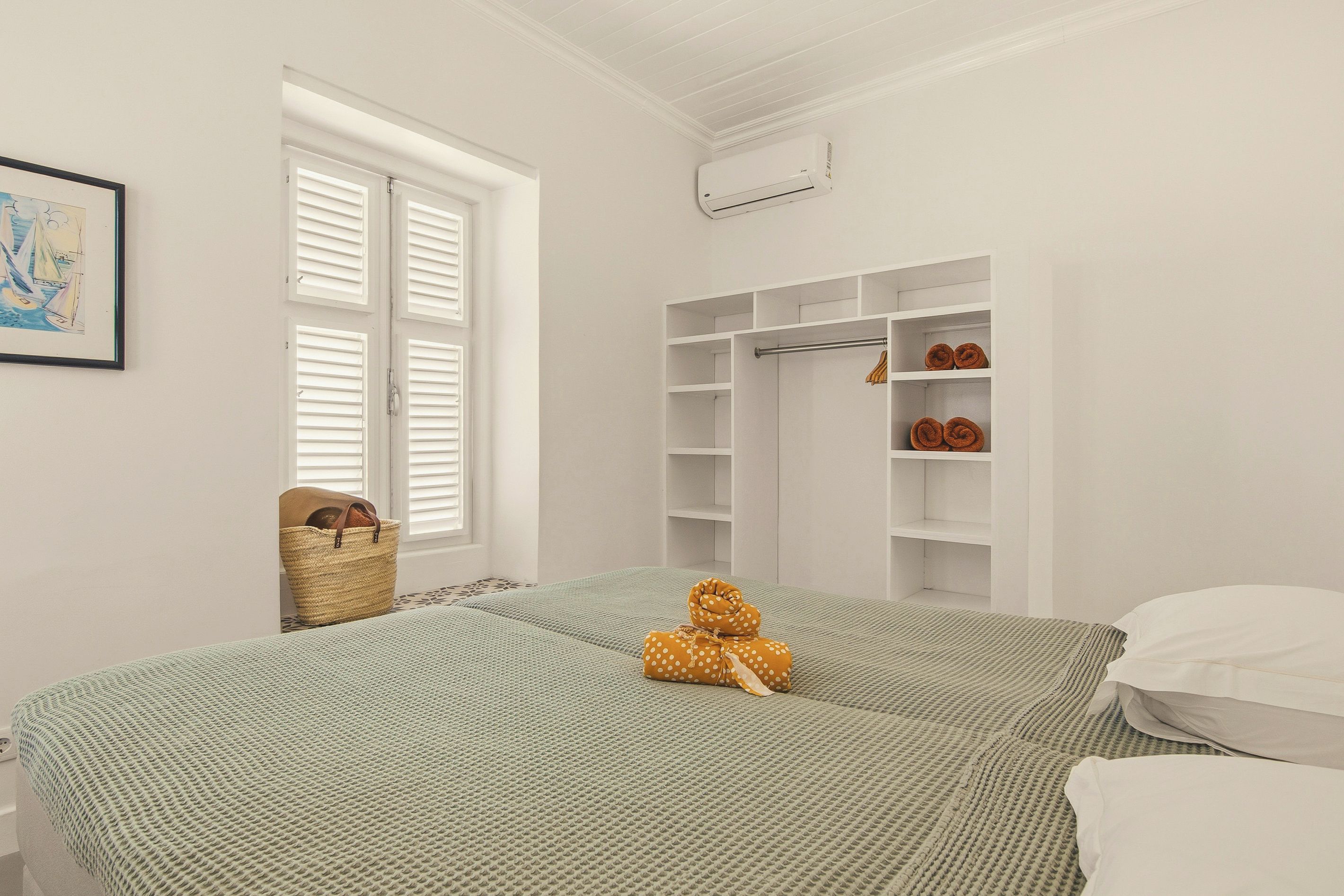 Een slaapkamer met twee bedden, een kledingkast, een raam met luiken en een wandairconditioner.