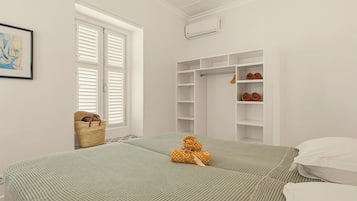 Een slaapkamer met twee bedden, een kledingkast, een raam met luiken en een wandairconditioner.