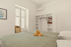 Quarto com duas camas, guarda-roupa, janela com persianas e ar condicionado fixado na parede.