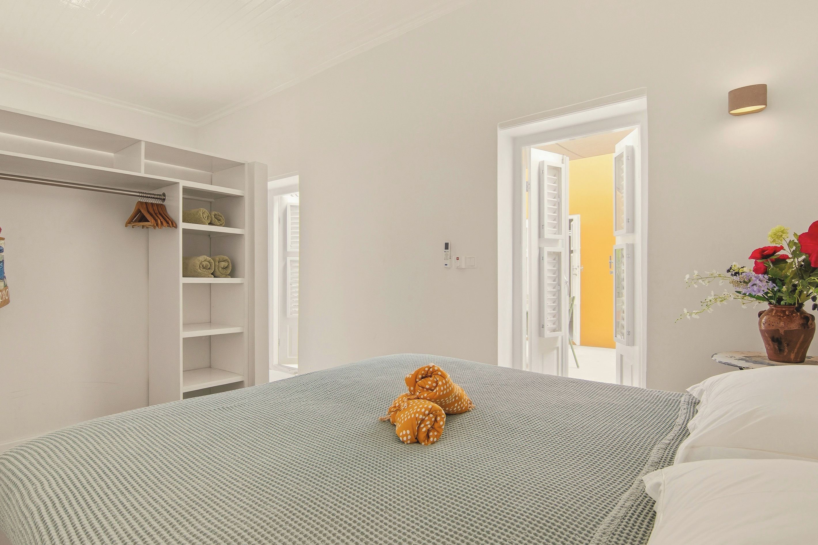 A bedroom with a bed, a closet with shelves, and a door leading to another room.