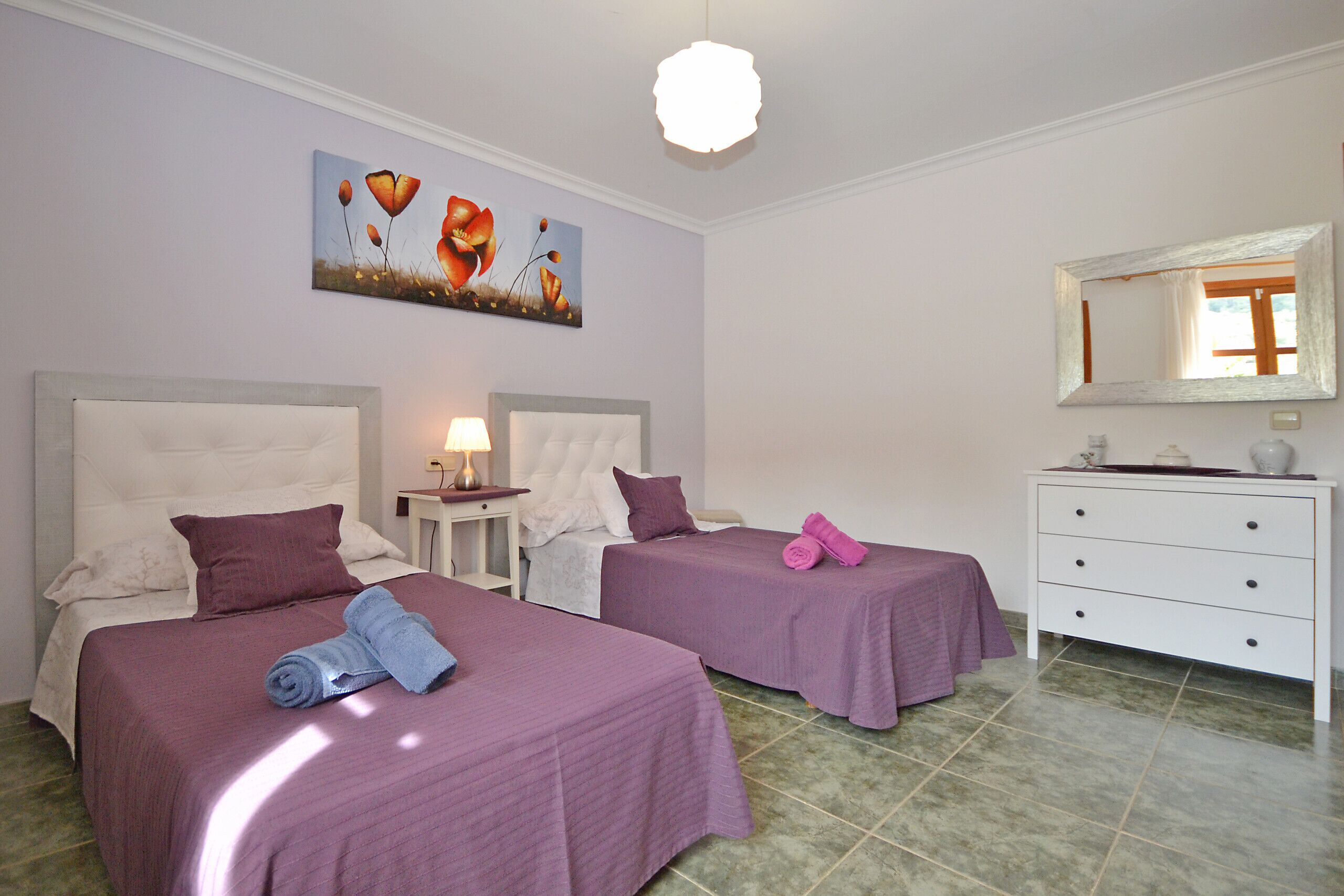 A hotel room with two beds, a nightstand, a dresser, and a painting on the wall.