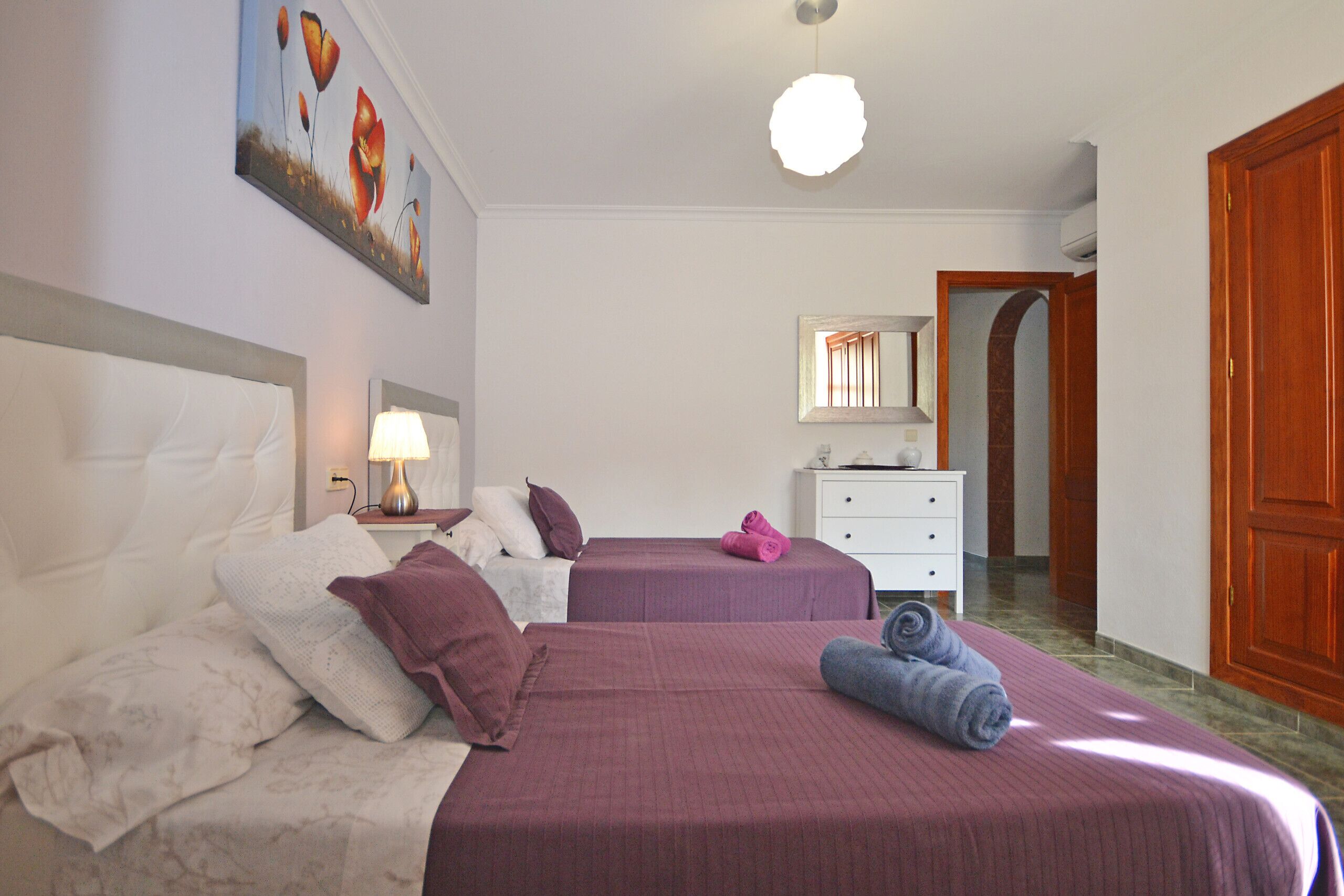 Habitació d'hotel amb dos llits, una nit falda amb una làmpada, un armari i una porta que condueix a una altra habitació.