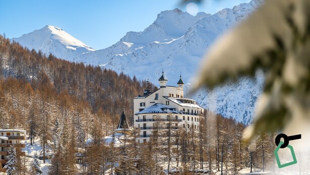 A snow-covered mountain landscape with a building featuring multiple towers and a central structure, surrounded by trees and snow. - Hotiday Sestriere Ski Run (Sestriere)