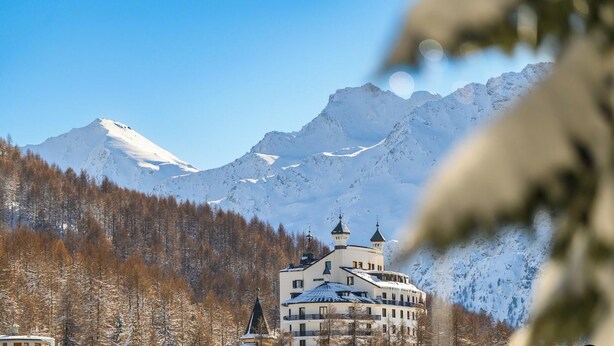 Un hotel con una montaña nevada al fondo, un área boscosa y un cielo despejado.