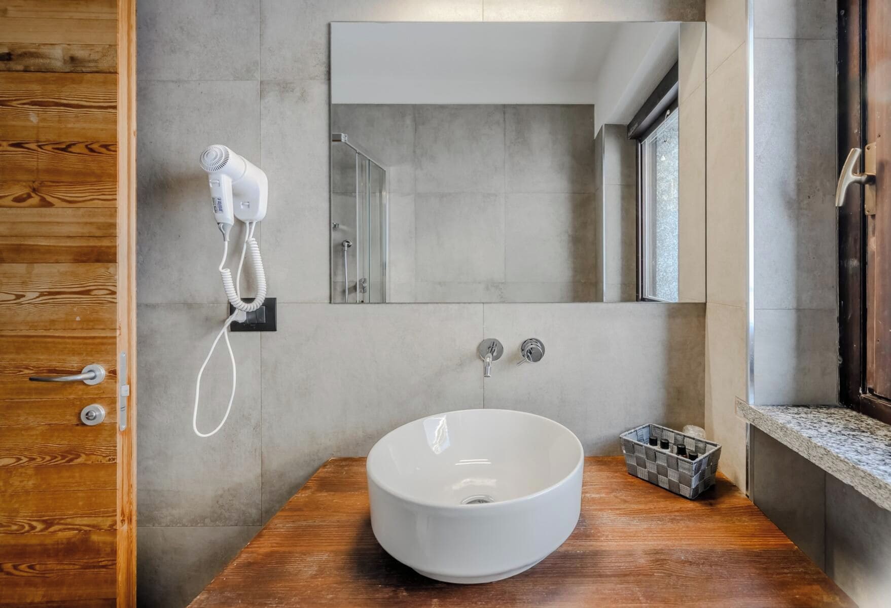 A modern bathroom with a large mirror, a white vessel sink, and a hairdryer on the wall.
