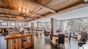A spacious restaurant with wooden ceilings and a central bar area. Tables are arranged for dining, and there are large windows providing views of the outdoors. - Hotiday Sestriere Ski Run (Sestriere)