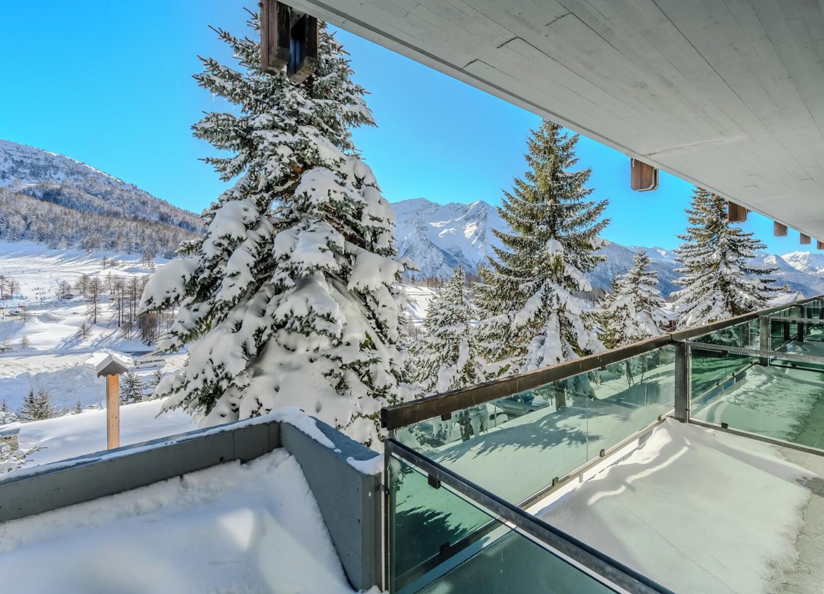 Un balcon doté d’une balustrade en verre, offrant une vue sur un paysage montagneux enneigé.