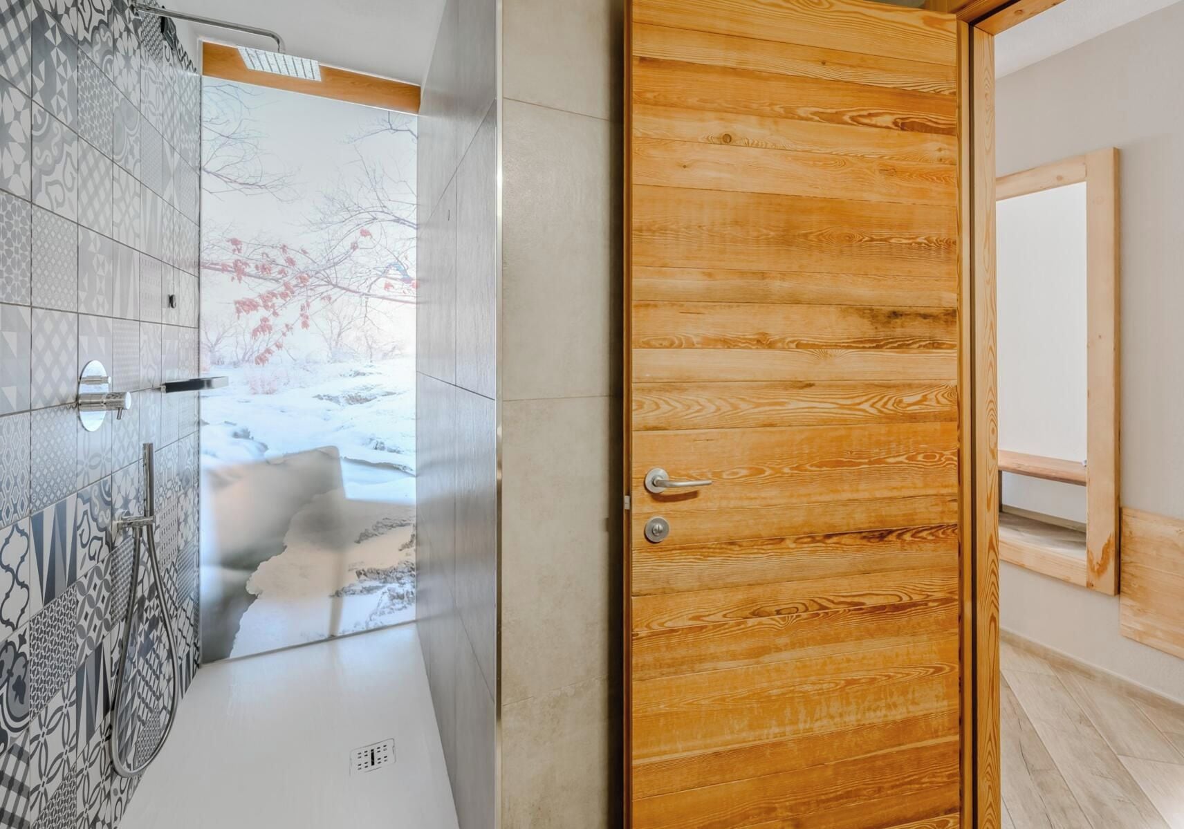 A bathroom with a patterned tile wall, a wooden door, and a mirror.
