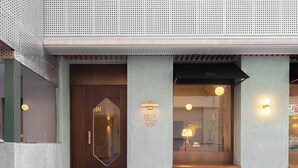 A modern building entrance with a wooden door, a bench, and two wall-mounted lights. - Mudita City Hotel (Xiamen)