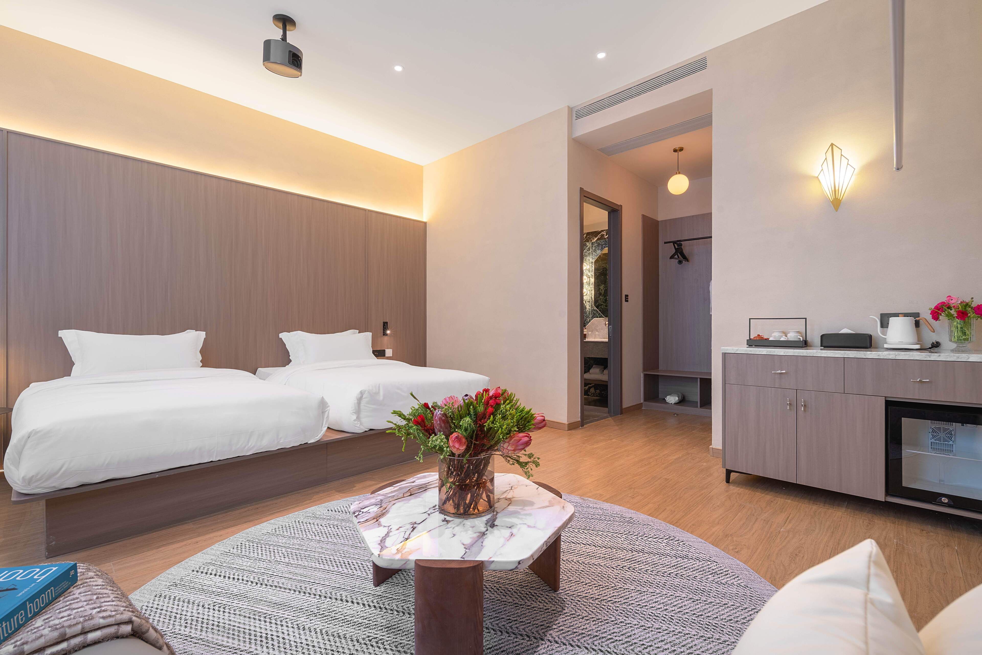 Una habitación de hotel moderna con una cama, una mesita con un jarrón de flores, un sofá y un mueble con microondas.