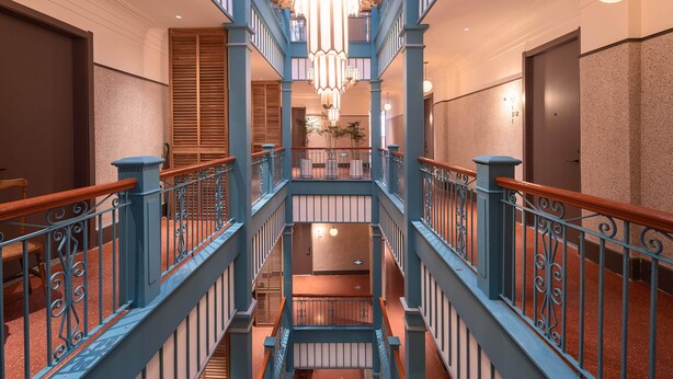 A multi-level interior with a central staircase, blue railings, and a large chandelier. - Mudita City Hotel (Xiamen)