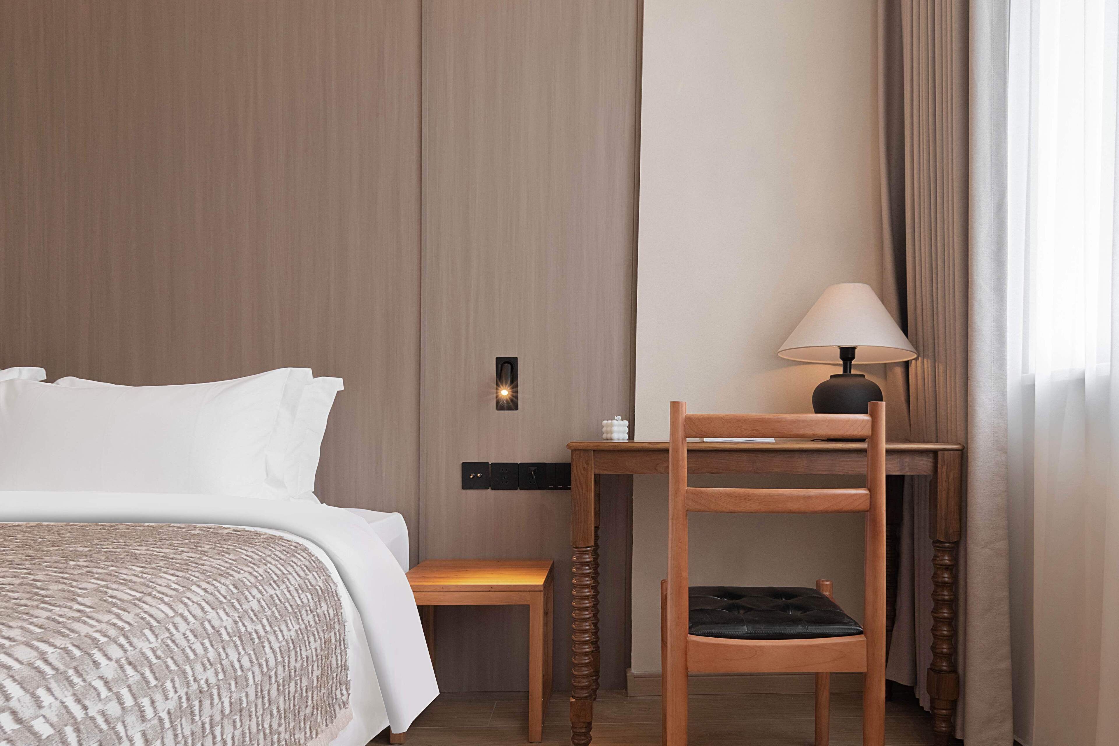 Una habitación de hotel con una cama, una silla de madera, una mesita y una lámpara.