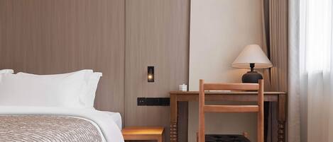 Una habitación de hotel con una cama, una silla de madera, una mesita y una lámpara.