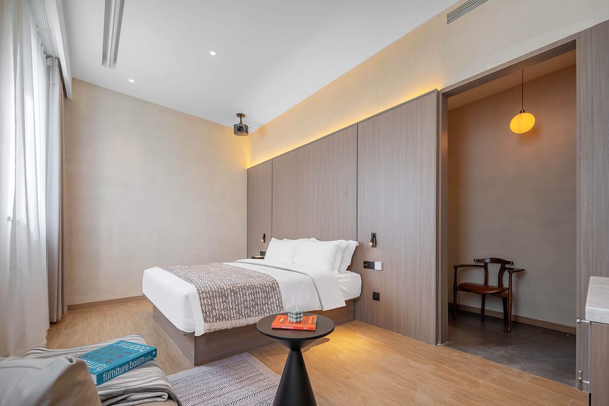 A modern hotel room with a neatly made bed, a small round table with a book, and a chair.