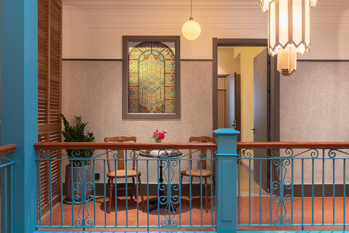 A balcony with a wrought iron railing, a stained glass window, and a table with chairs.