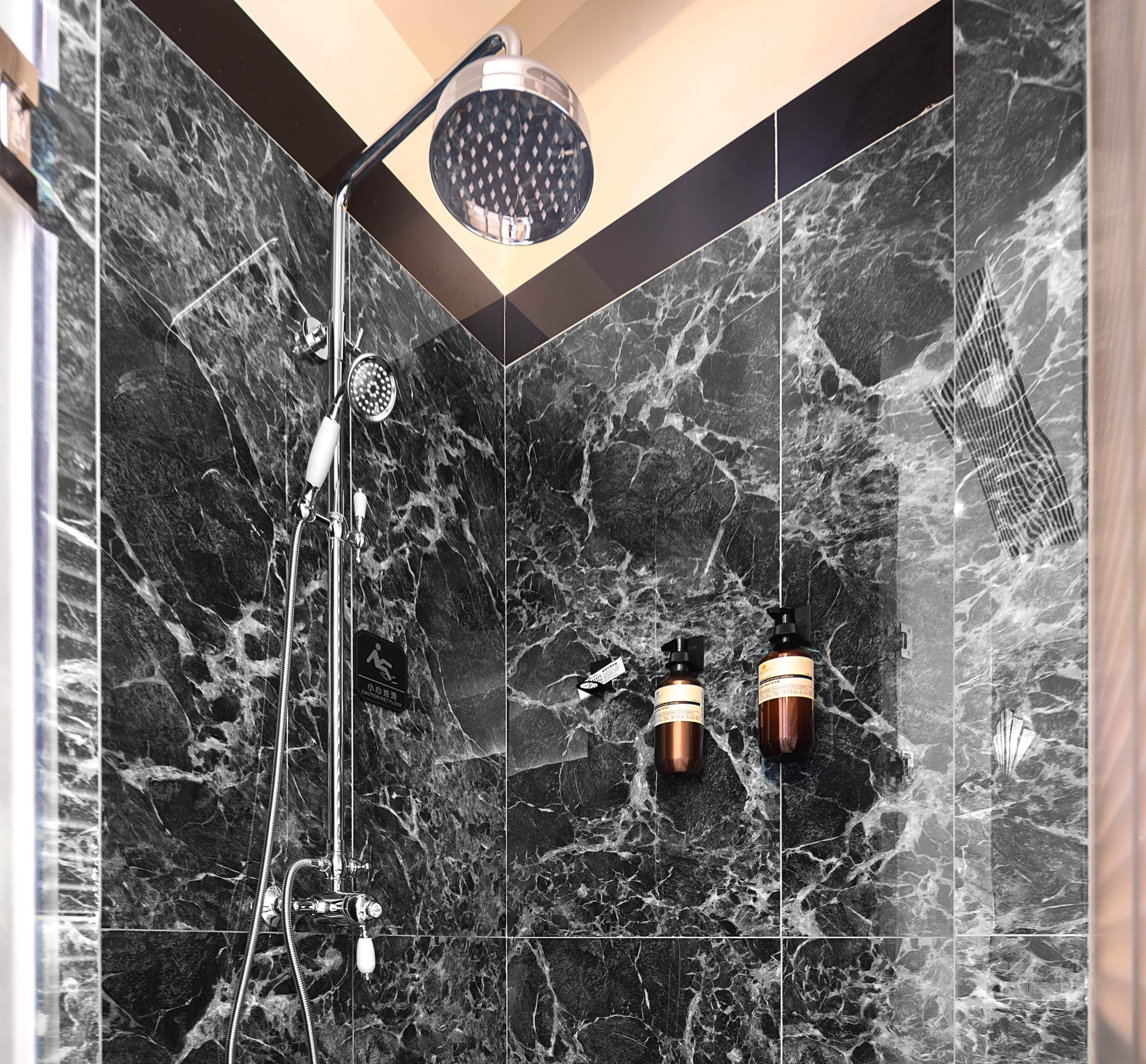 Une salle de bain avec des carreaux de marbre noir, une douche équipée d’un pommeau de douche amovible et deux bouteilles de shampoing.