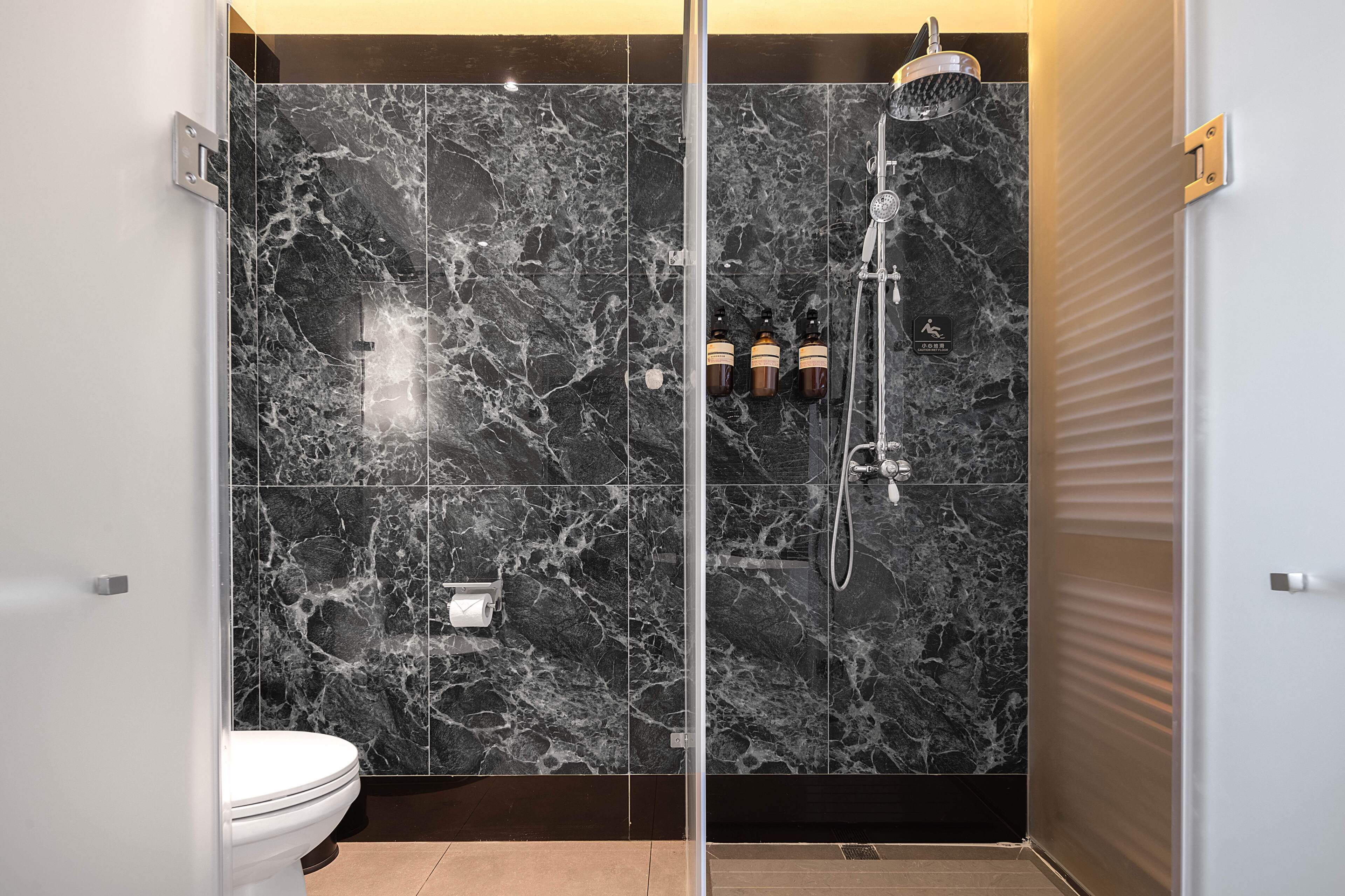 A modern bathroom with a glass-enclosed shower, marble walls, and a toilet.