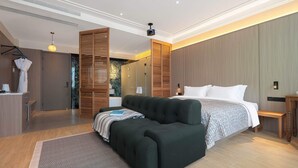 A modern bedroom with a large bed, a dark green sofa, and a wooden wardrobe. - Mudita City Hotel (Xiamen)