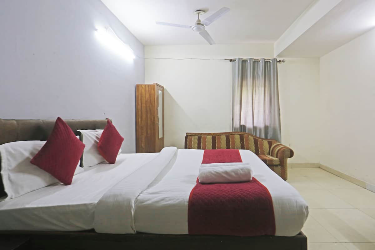 A hotel room with a bed, a chair, a wardrobe, and a ceiling fan.