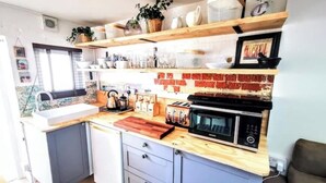 A compact kitchen with a wooden countertop, a built-in microwave, and a toaster. There are shelves above the counter holding various kitchen items.