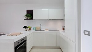 A modern kitchen with white cabinetry, a built-in oven, a countertop with a rolling pin, and a small plant on a shelf.