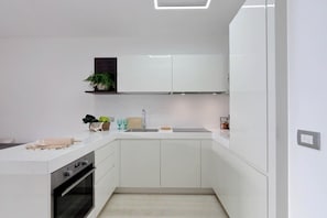 A modern kitchen with white cabinetry, a built-in oven, a countertop with a rolling pin, and a small plant on a shelf.