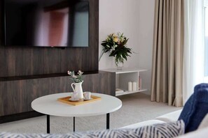 En moderne stue med et fladskærms-tv monteret på væggen, et rundt sofabord med en bakke, en vase med blomster og en sofa.