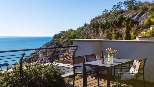 A terrace with a table and chairs, overlooking a coastal landscape.