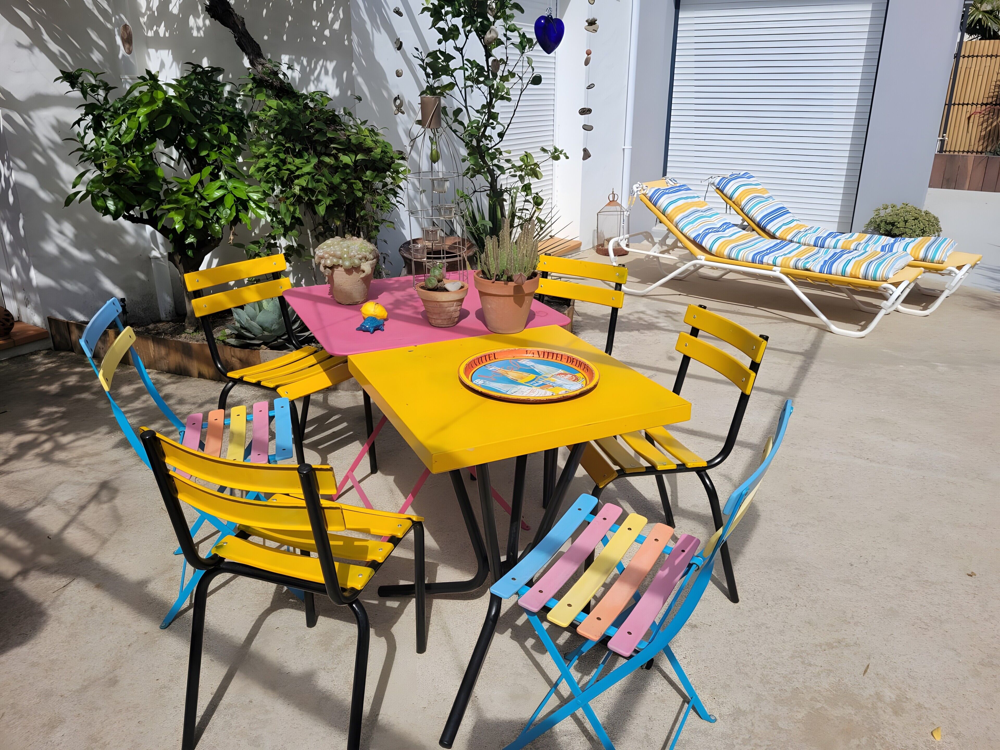 Un espace patio avec une table jaune, des chaises colorées et des fauteuils avec des coussins à rayures.
