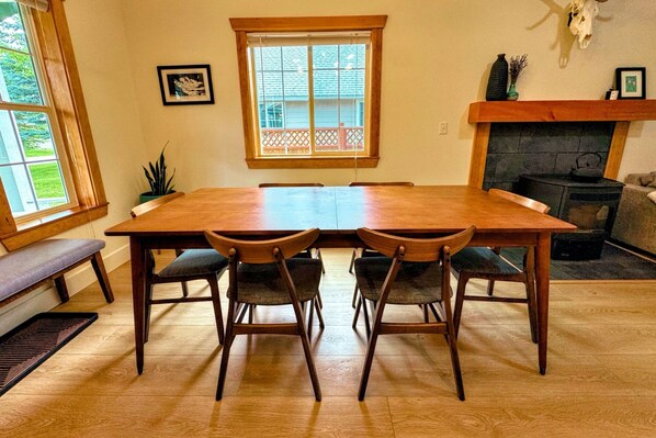 A dining area with a wooden table and four chairs, a fireplace, a window with a view, and a bench.