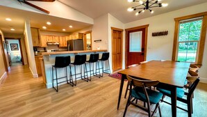 A spacious kitchen with wooden cabinets and a central island, a dining area with a large wooden table and chairs, and a view of the outdoors through a large window. - Cozy 3BR/2BA Family Retreat in Driggs (Driggs)