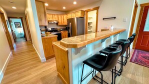 A modern kitchen with wooden cabinets, a stainless steel refrigerator, a granite countertop, and black bar stools. - Cozy 3BR/2BA Family Retreat in Driggs (Driggs)