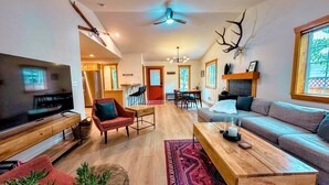 A spacious living room with a large TV, a sofa, a coffee table, and a dining area with chairs and a table. - Cozy 3BR/2BA Family Retreat in Driggs (Driggs)