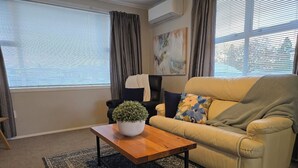 A living room with a beige sofa, a wooden coffee table with a potted plant, and a patterned rug. - Charming 3-bedroom house in Papakura 20min from Airport (Auckland)