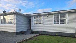 A single-story house with a front porch, a chimney, and a small front yard with a gravel pathway and grass. - Charming 3-bedroom house in Papakura 20min from Airport (Auckland)