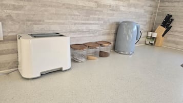 Une cuisine avec un grille-pain blanc, une bouilloire argentée et trois bocaux avec des couvercles.