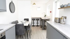 Une cuisine moderne avec un coin repas, dotée d’un parquet en bois clair, de meubles de rangement gris et d’un plan de travail blanc.