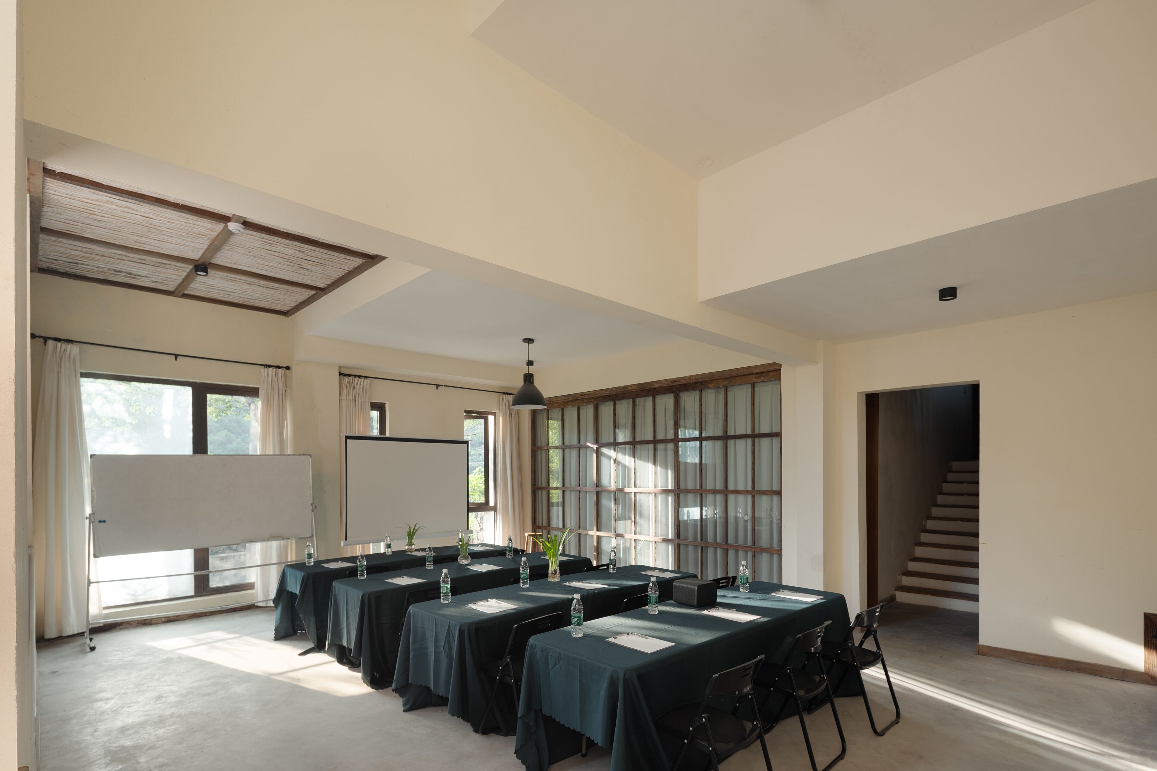 Un salón de conferencias con mesas, sillas, una pizarra y ventanas amplias.