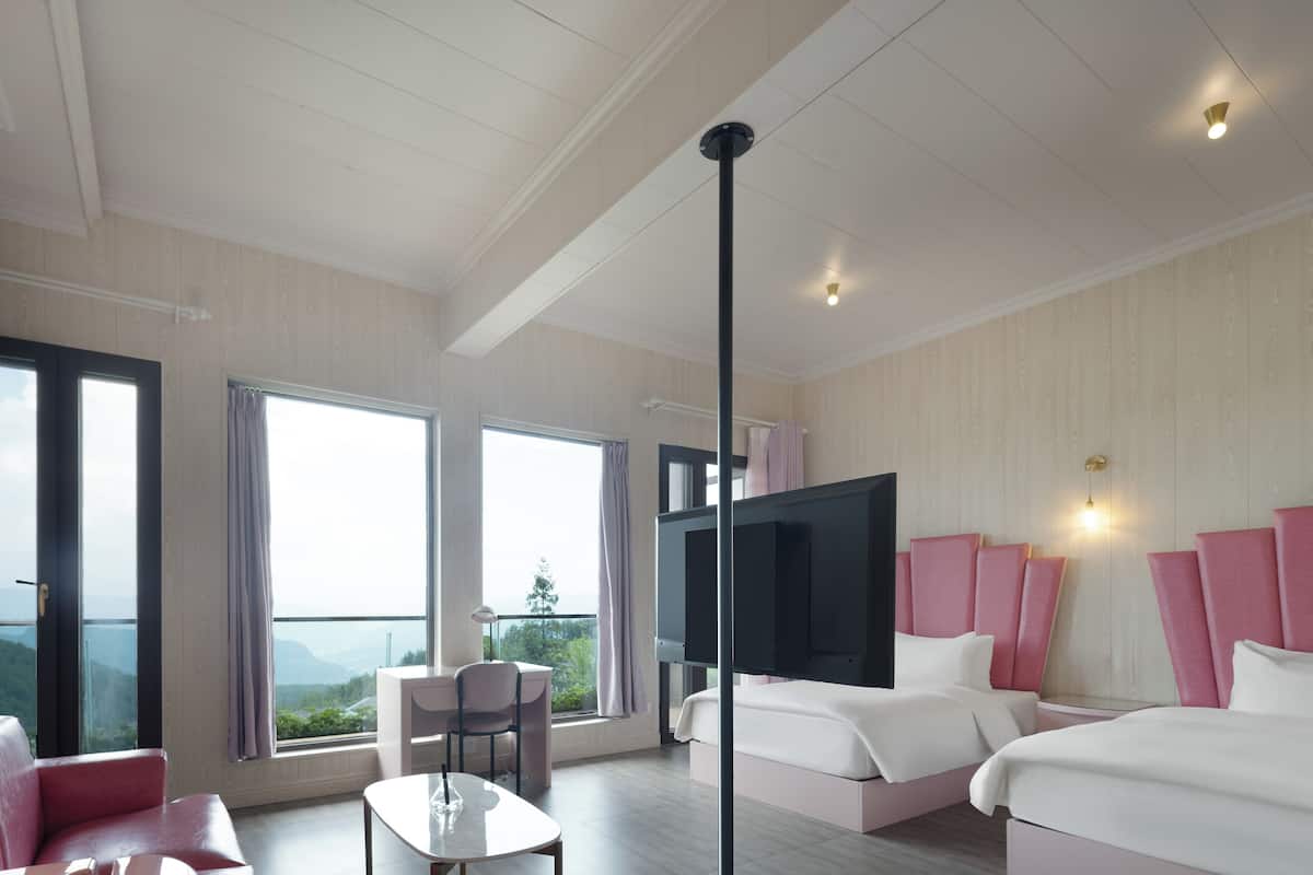 Ein Hotelzimmer mit zwei Betten, einem Fernseher, einem Schreibtisch mit Stuhl und großen Fenstern mit Blick ins Freie.