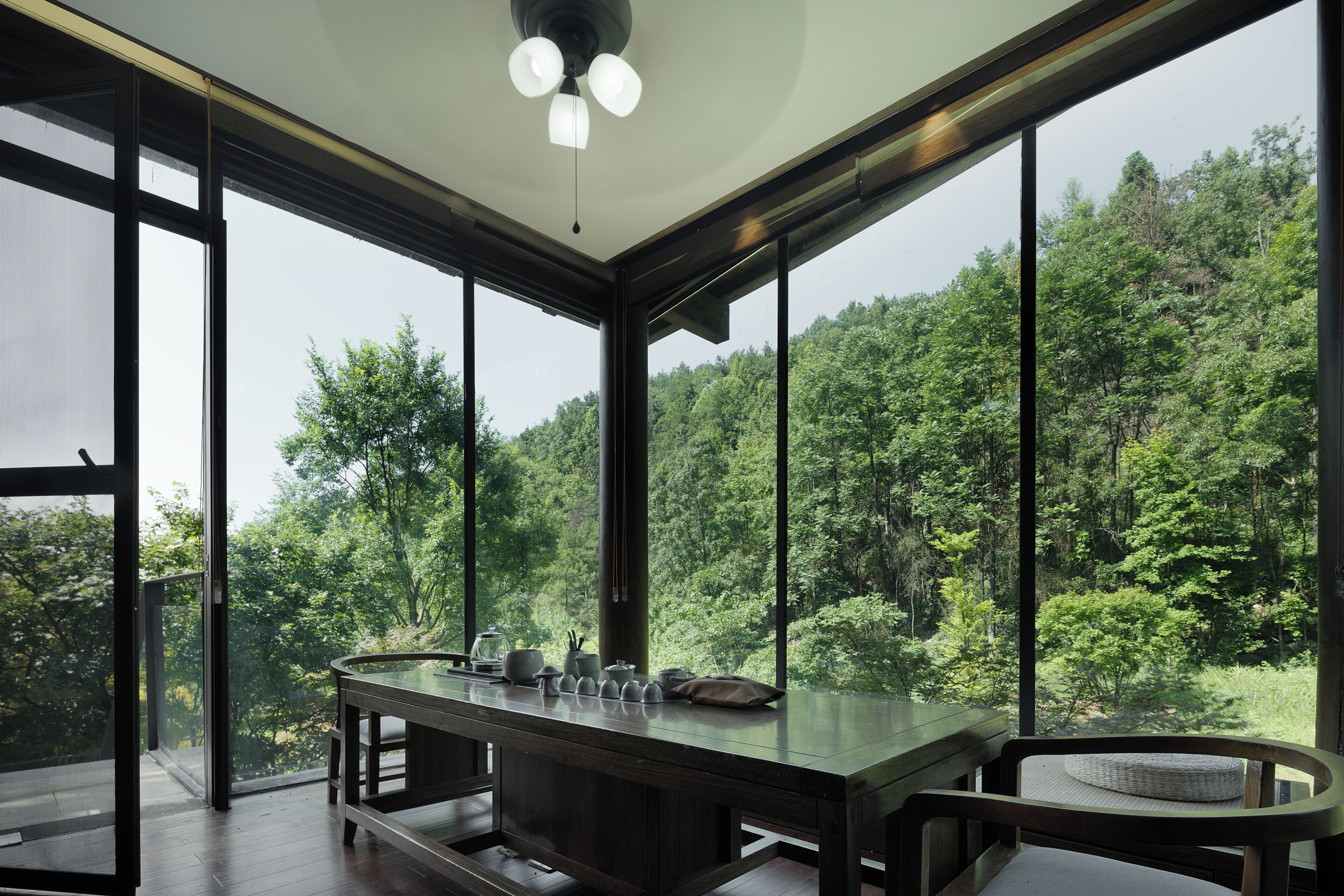 A modern room with large windows, a wooden table, and a view of a forested area.