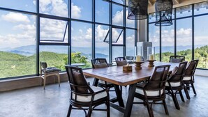 Un espace repas comprenant une grande table et des chaises, de grandes fenêtres offrant une vue sur les montagnes et des luminaires suspendus.