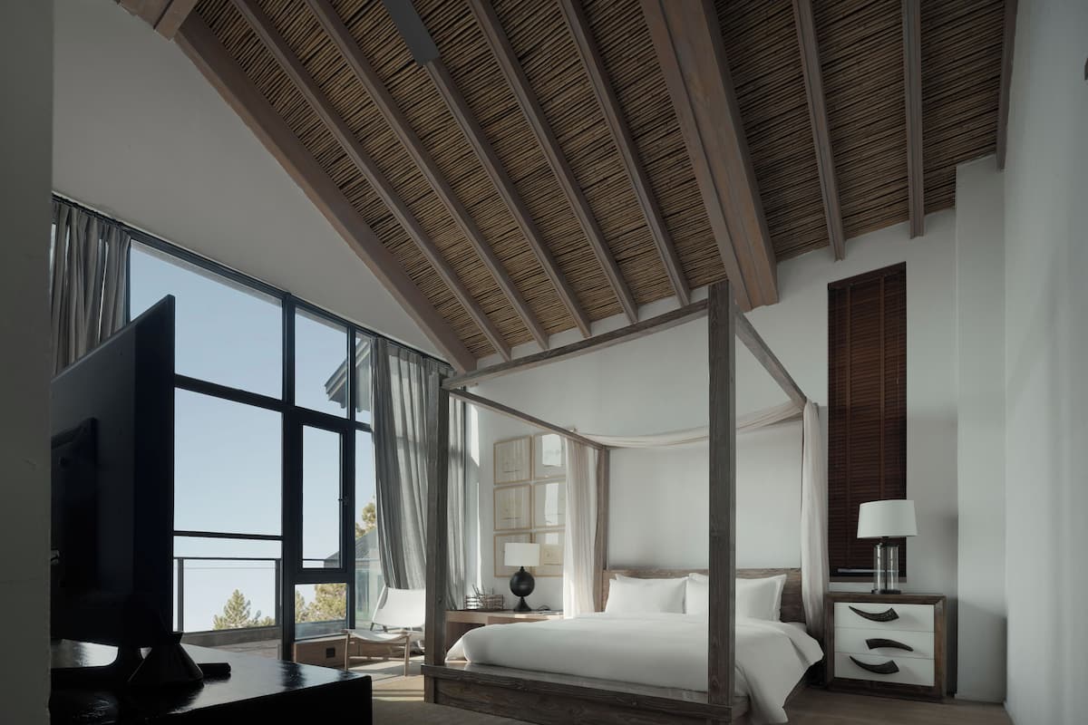 Ein modernes Schlafzimmer mit Himmelbett, großen Fenstern und einer Decke mit Holzbalken.
