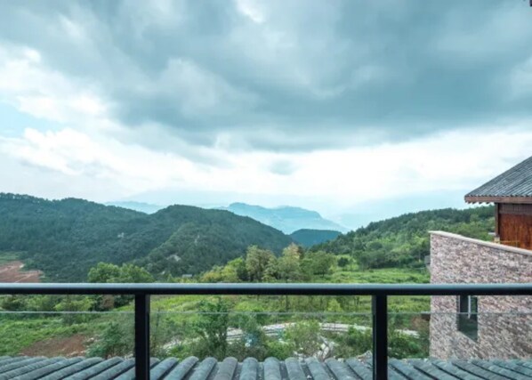 A view from a balcony overlooking a mountainous landscape with a stone building to the right.