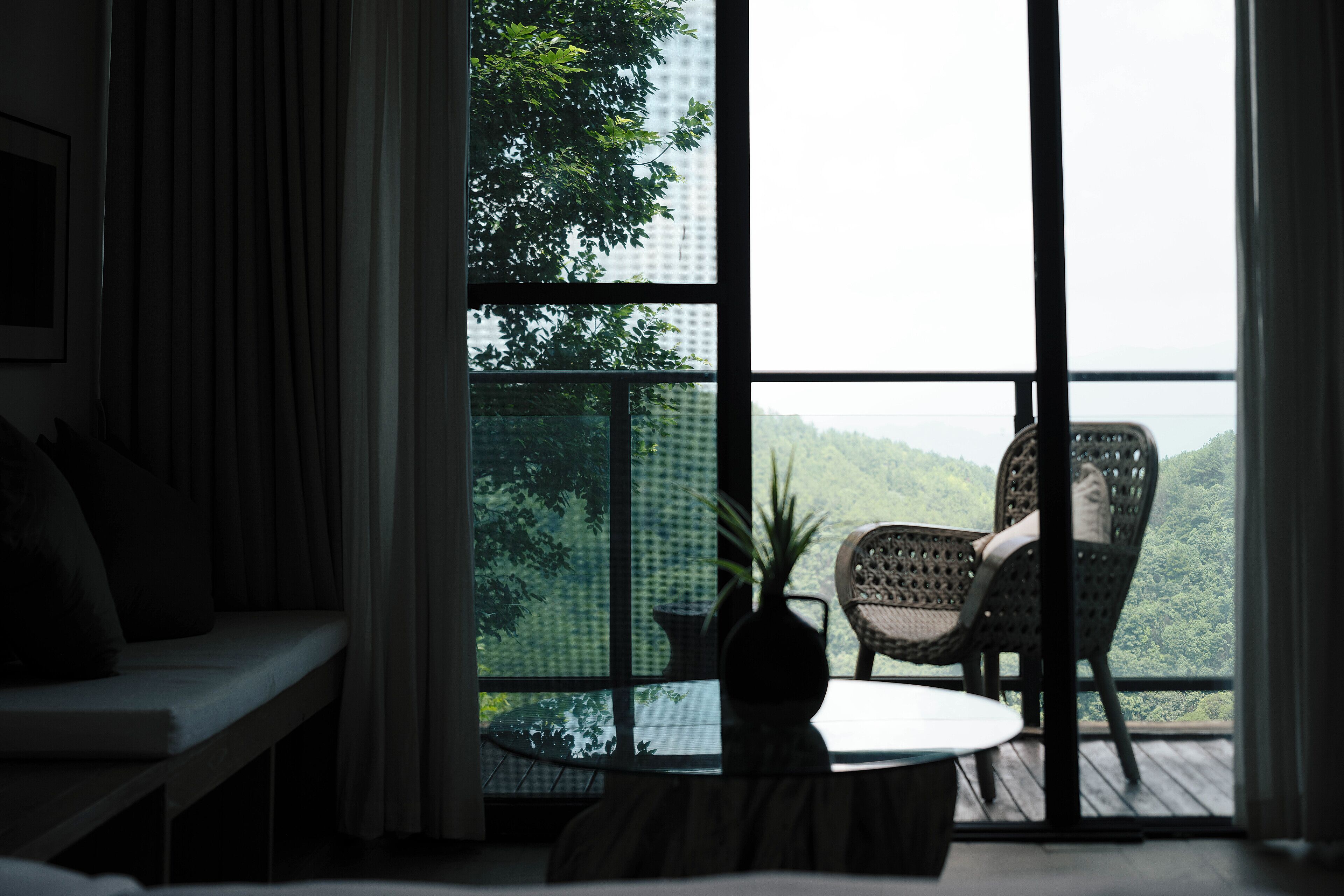 A room with a large window, a chair, a small table, and a plant.