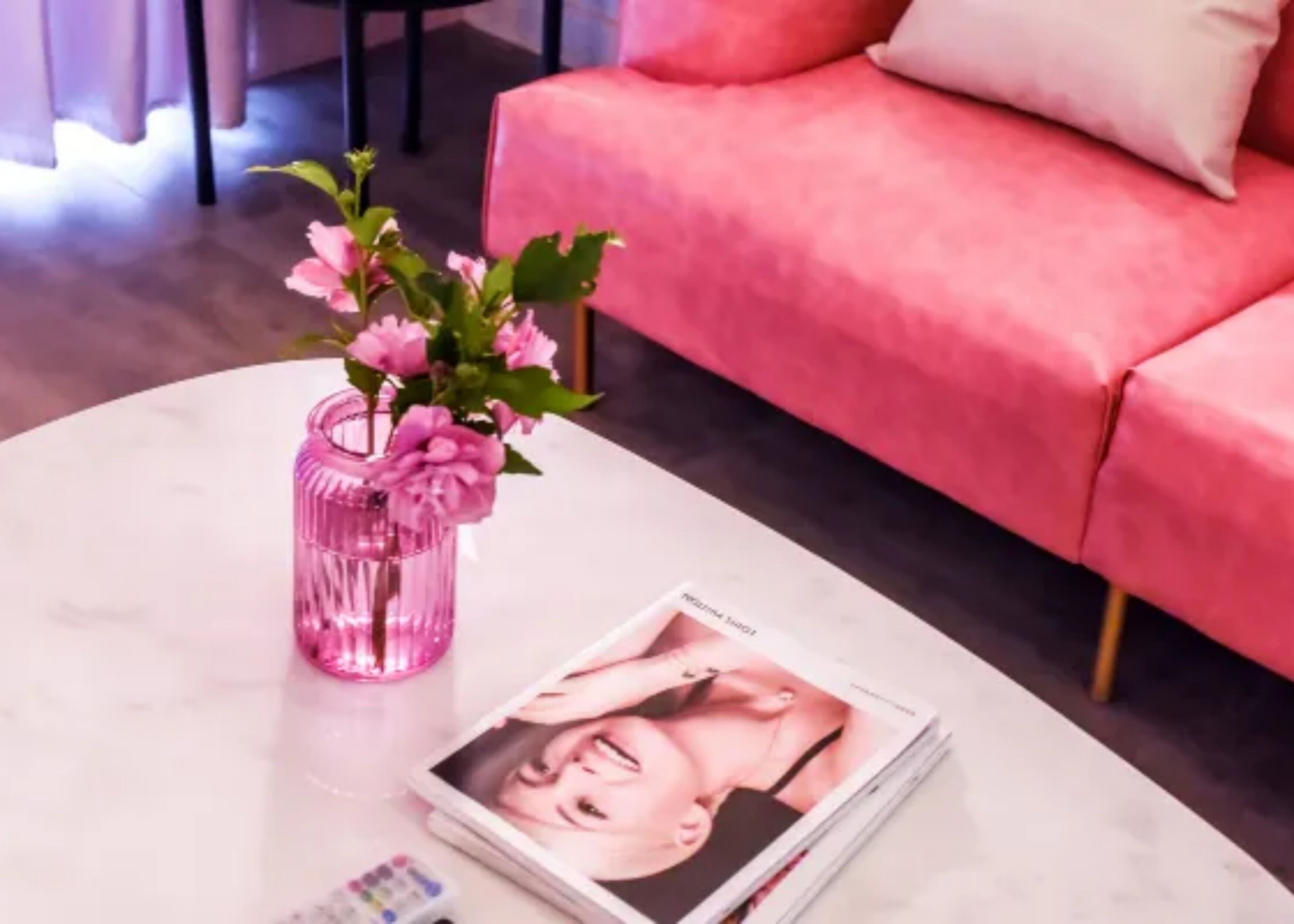 Un sofá rosa, una mesa de centro blanca y un florero rosa con flores.