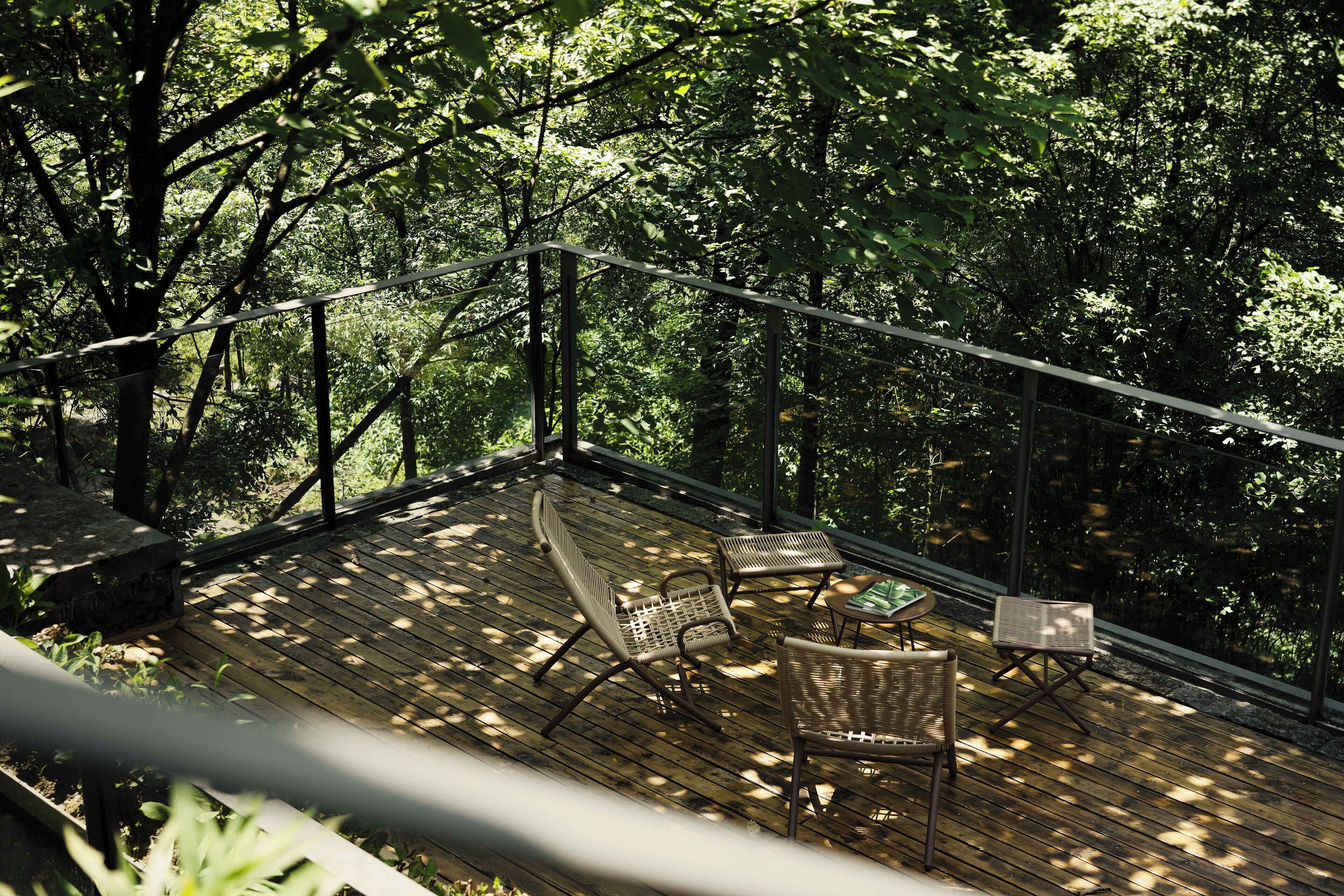 A wooden deck with outdoor furniture, surrounded by dense trees.