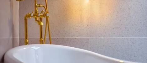 A bathroom with a freestanding bathtub, a gold-colored showerhead, and a wall-mounted light fixture.